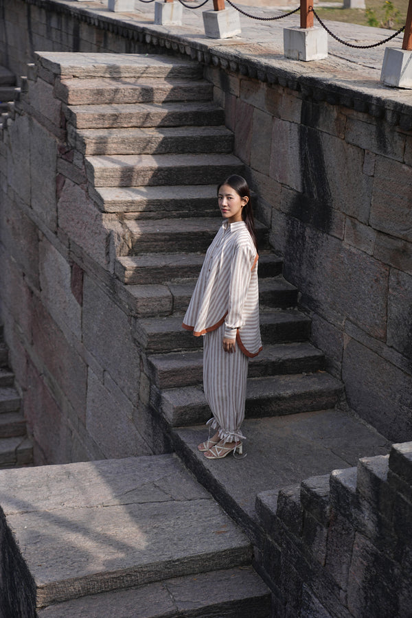 Woman wearing the Sutra Arc Stripe co-ord — a striped cotton button-down shirt with matching ruffled-hem trousers